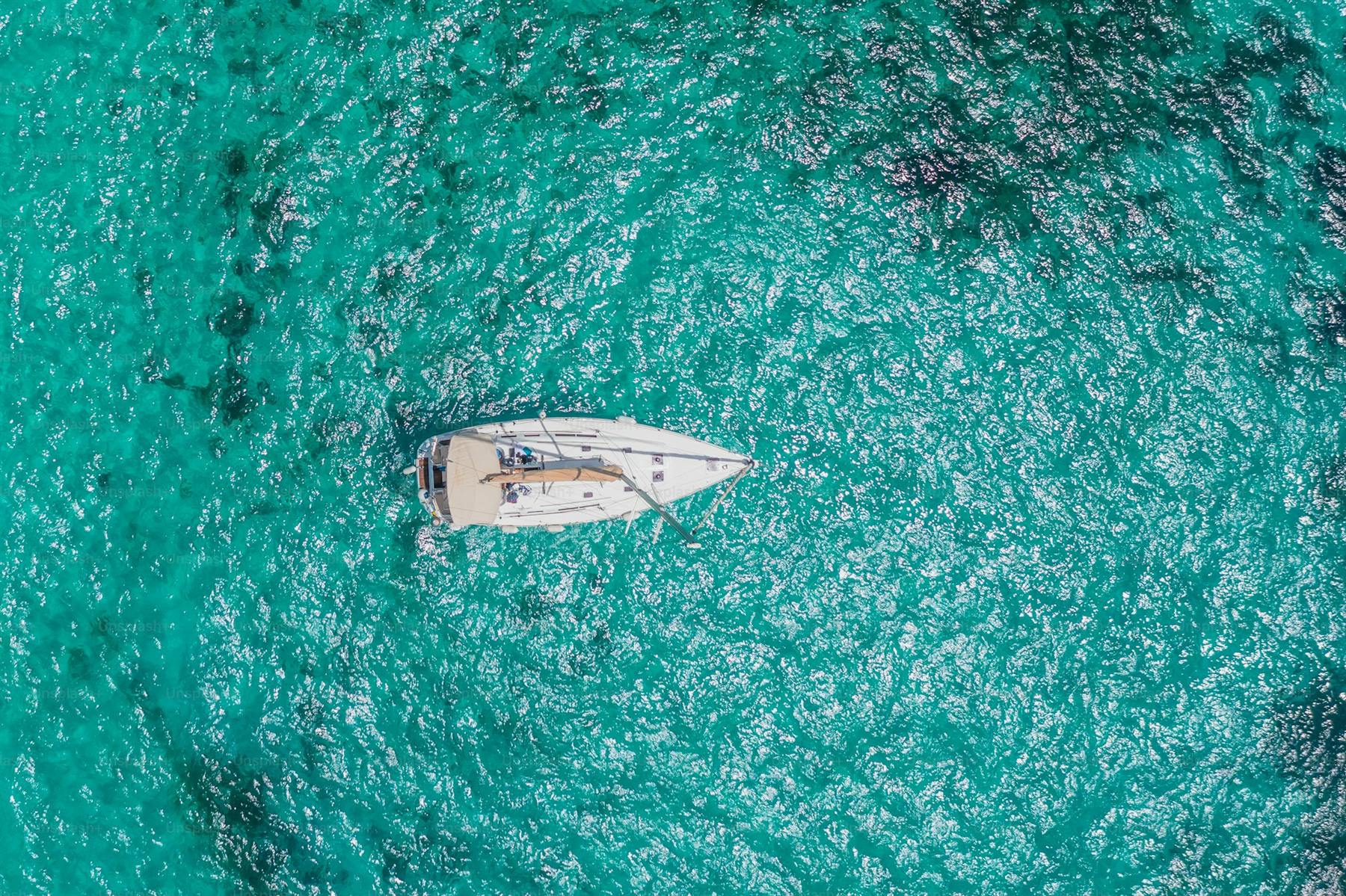 A yacht alone in brilliant turquoise water, seen from above