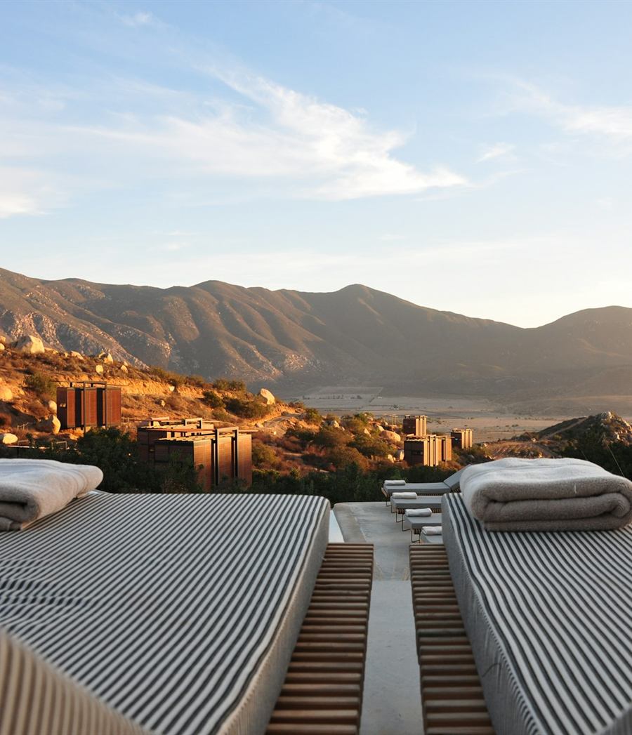 Two loungers with folded towels on a terrace above dry mountains at golden hour
