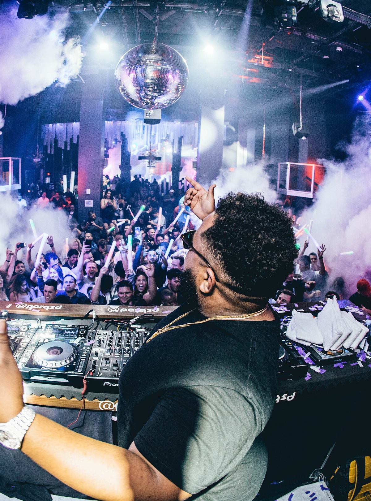 A packed dance floor beneath a mirrorball, smoke over the crowd
