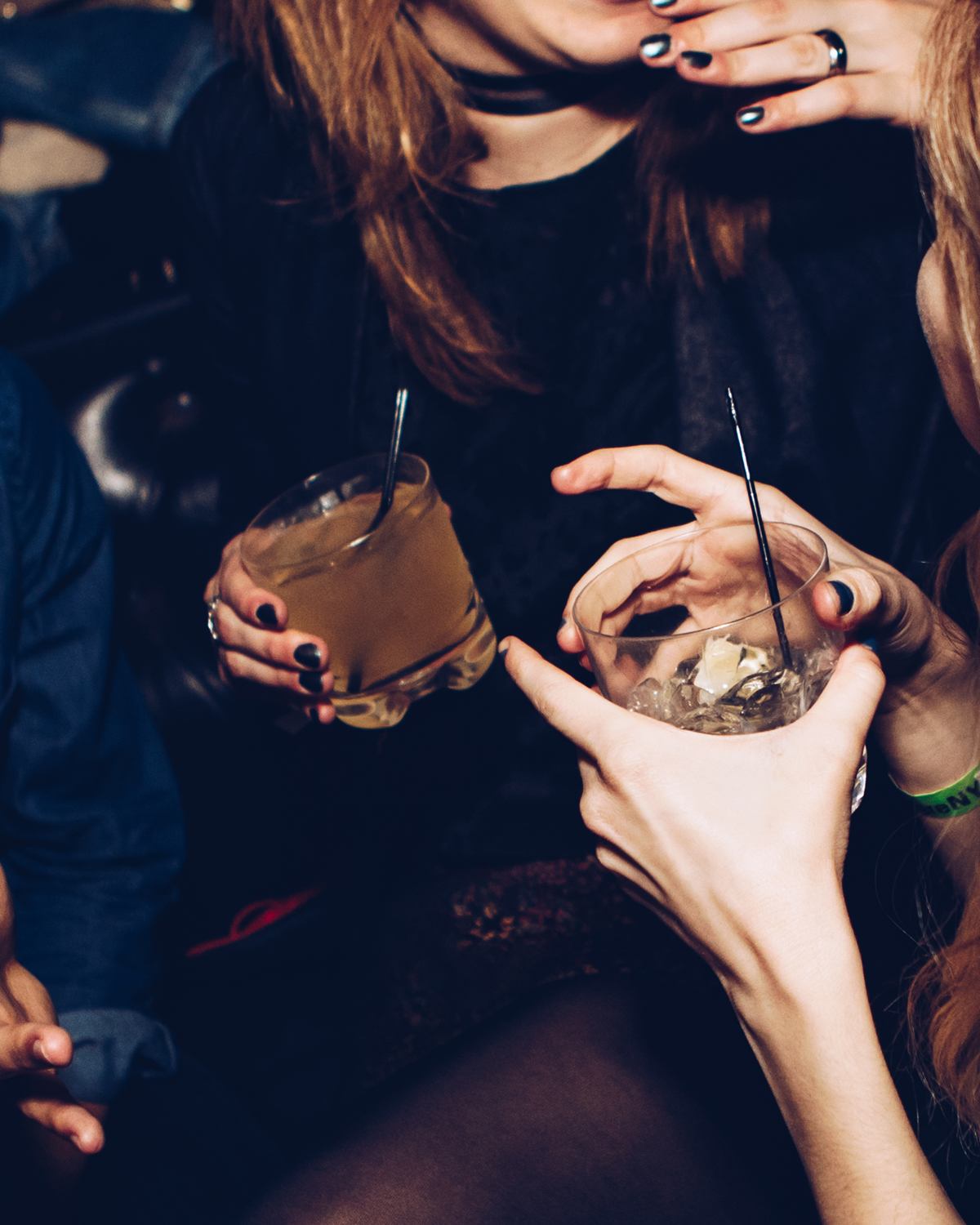 Hands holding cocktails in a dark booth late at night